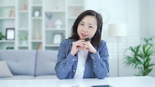 Webcam view. Confident asian woman in headset talking on video call looking at camera while sitting