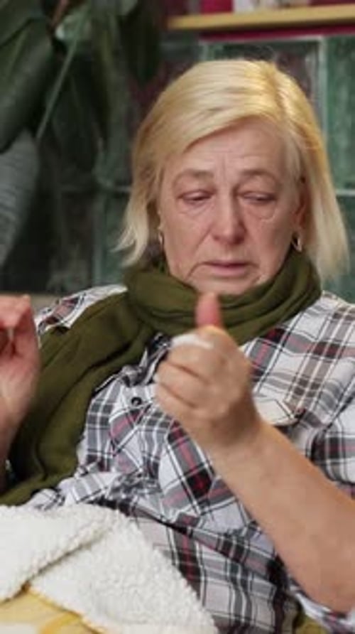 Несчастная старушка кладет бумажное полотенце на стол Портрет пожилой женщины, лежащей на сером диване под