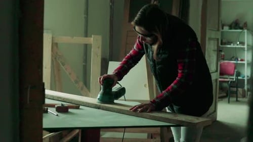 Young woman craftsman grinding wood in her carpentry workshop