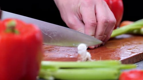 Spring onion is cut by knife on wooden chopping board surrounded by various vegetables