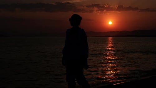 Woman Walking Towards Setting Sun on Beach