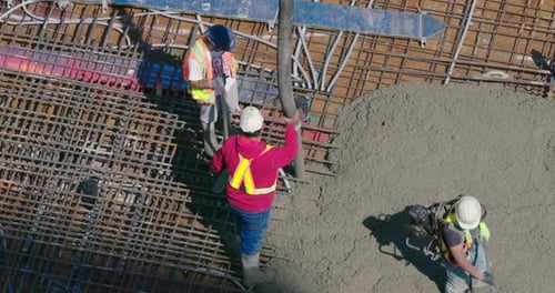 Vista superior de trabajadores de la construcción vertiendo cemento en el techo de un edificio.