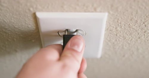 Gros plan de la main d'un homme branchant le cordon dans une prise électrique puis le débranchant au ralenti