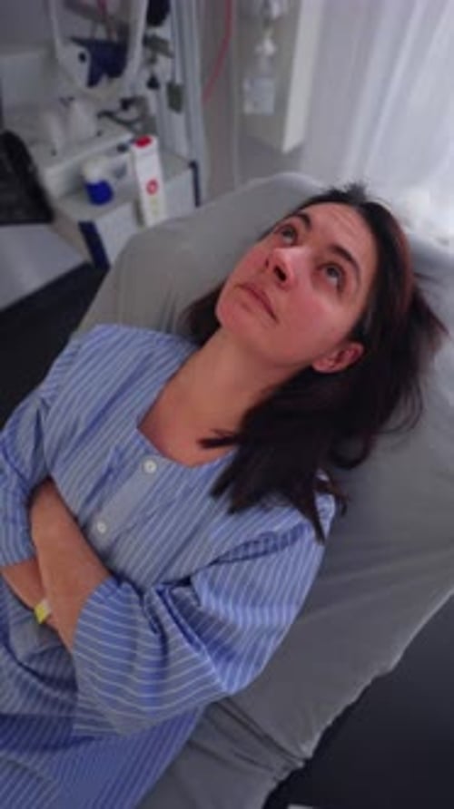Female patient lying back on hospital bed looking upward with serious expression before surgery,