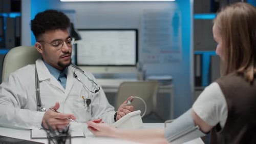 Médico general masculino que mide la presión arterial de una mujer en la clínica
