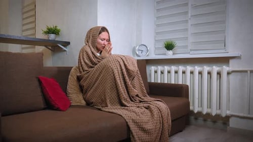 Femme essayant de se réchauffer assise enveloppée dans une couverture à la maison sans chauffage