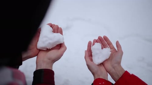 Couple Holding Heart-Shaped Snowballs on Winter Day