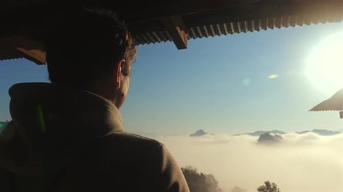 Mann steht auf dem Balkon und betrachtet den malerischen Sonnenaufgang oder Sonnenuntergang über einer Wolke