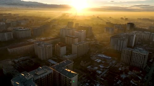 Aerial panoramic view of city buildings shrouded in morning fog and golden light