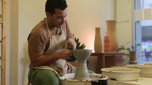 Male craftsman slow motion forming clay vase sculpture on workshop pottery wheel