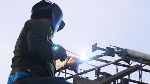Construction worker man in welding hood working on scaffolding at height at construction site