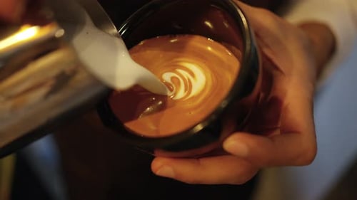 4K Close up of Barista hand pouring froth milk in espresso coffee making coffee latte in coffee cup.