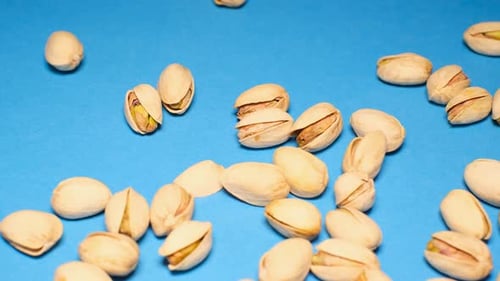 Pistachios Falling on Blue Surface, Close Up