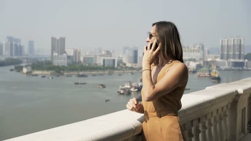 Young, Pretty Woman Talking on Cellphone Standing on Terrace in City 30s