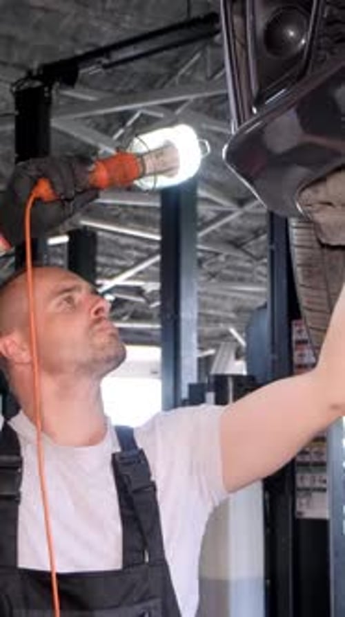Vídeo vertical: um mecânico embaixo de um carro na garagem usando roupas de trabalho e chapéu