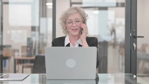 Senior Woman Answers Phone at Desk in Office