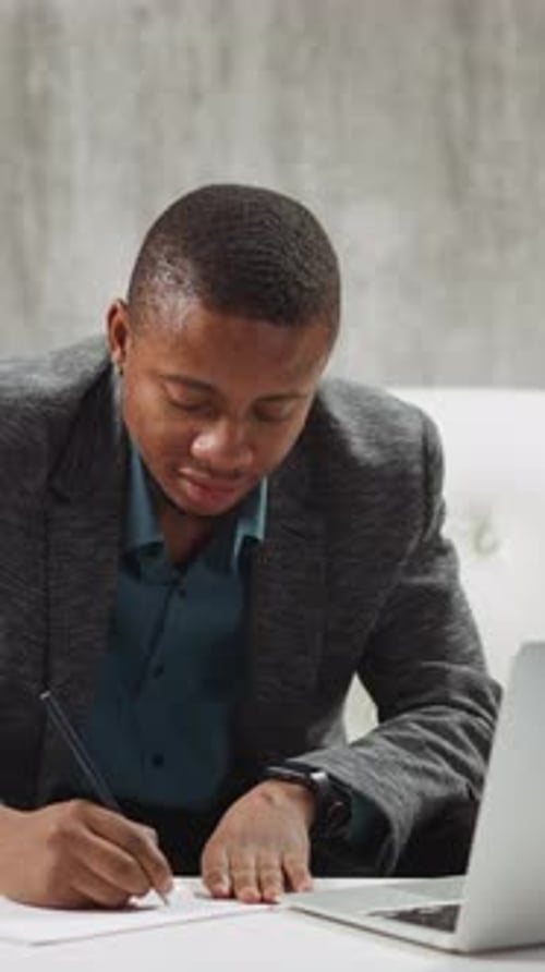 Man Writes on Paper near Laptop