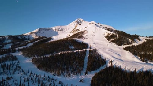A drone shot of snowy Big Sky, Montana in winter, showcasing the ski resort and majestic mountain te
