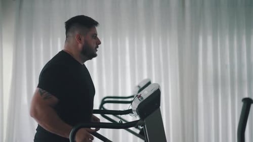 Homem forte treinando exercícios cardiovasculares na esteira na vista lateral da academia