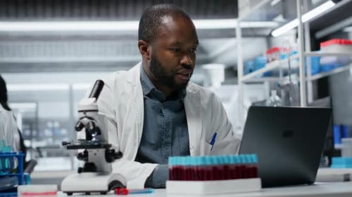 Scientist Analyzing Samples While Using Laptop in Lab