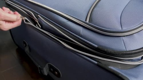 Hand Zipping Suitcase Closed on Wooden Floor