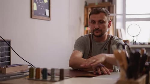 Craftsman Unrolls Natural Leather Sheet at Table in Workshop