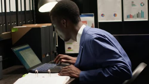 Man Working Late at Desk with Laptop and Documents