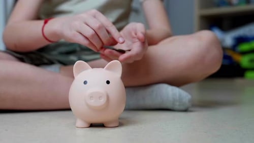 Die Hände eines Kindes steckten angesammeltes Geld in ein Sparschwein.