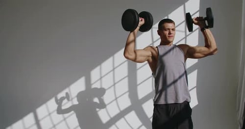 Athletic man has workout and lifting dumbbells in studio with white background