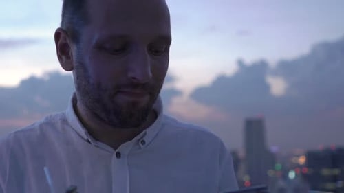 Young man enjoying cocktail and smartphone on luxury rooftop terrace bar