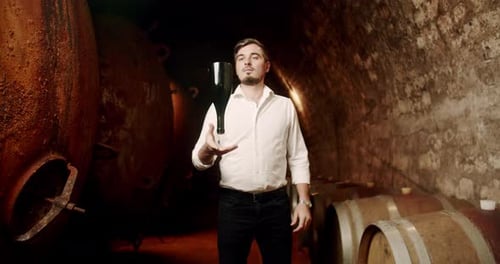 Man with the Wine Bottle in a Factory Old Cellar with Many Wooden Barrels