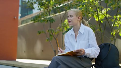 Blonde Woman Writes in Notebook Outdoors on Bench