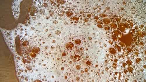 Beer alcoholic beverage up-close bubbles foam, amber dark brown homemade drink