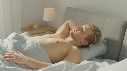Man Waking Up and Stretching in Sunny Bedroom