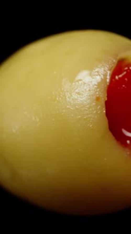 Vertical video. One Brined Green Olive Stuffed with Pepper Rotates on a Black Background.