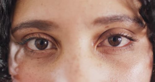 Close up portrait of the opening eyes of biracial woman looking to camera, smiling in slow motion