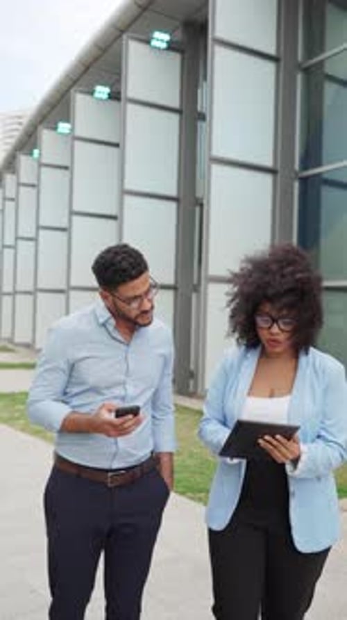 two diverse Business colleagues walking and discussing work using tablet and phone outside office