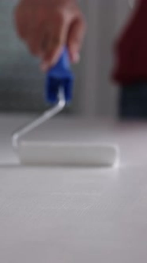 Hand using Paint Roller to Apply White Paint