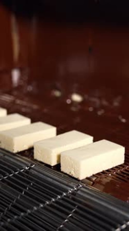 White candies move on the conveyor line to the flow of chocolate. Manufacture of chocolate candies