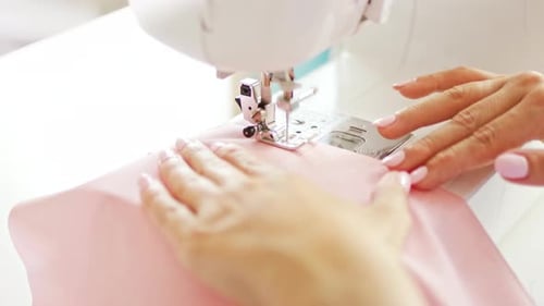 Woman clothing designer sews pink fabrics on a sewing machine. Needlework and handmade patchwork