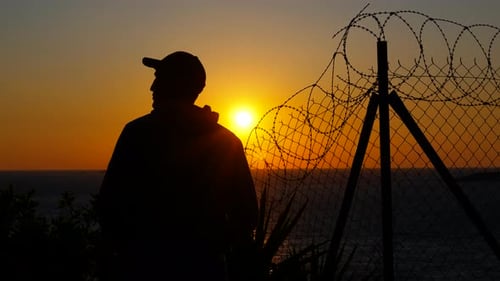 Refugee Observing Sunset Behind Barbed Wire Fence