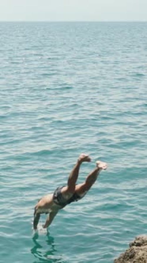 A man in a mask with a tattoo jumps into the sea from a cliff. Slow motion Vertical, Social Media.