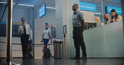 Airport Security Guard Watches as Crew Members Pass