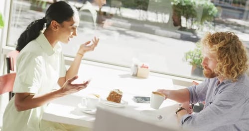 Happy diverse couple drinking coffee and talking at a table in cafe