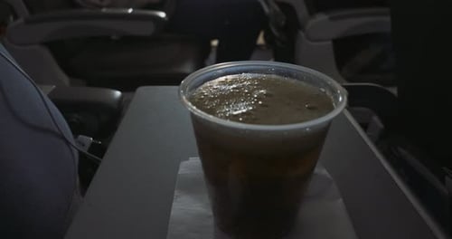 Close up of a plastic cup on an airplane, soda being pored.