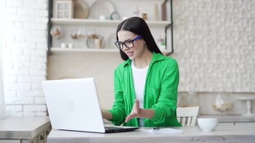 Young woman with eyeglasses sit in the light kitchen feels annoyed having problems with laptop.