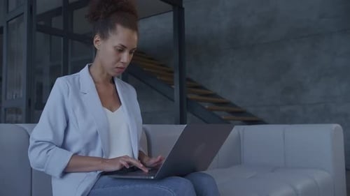 Jeune femme d'affaires afro-américaine adulte en costume bleu travaillant sur un ordinateur portable dans un loft à aire ouverte