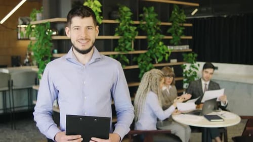 Smiling Man Stands in Front of Team Meeting