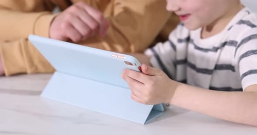 Father and his son using tablet at white table indoors, closeup