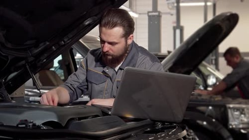 Focused Car Service Worker Using Laptop While Inspecting Engine